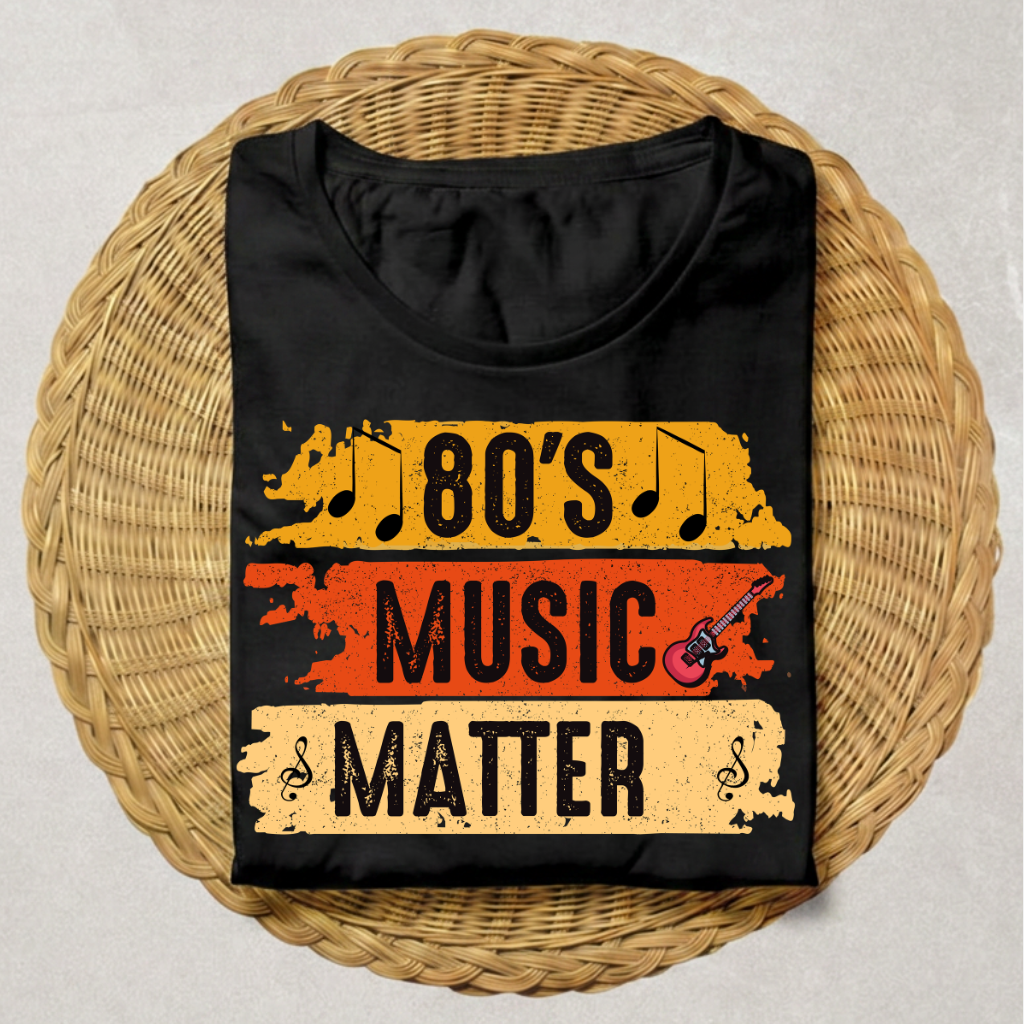 A black short-sleeve T-shirt laid flat on a round woven wicker tray, featuring a distressed retro graphic that reads '80's MUSIC MATTER' with musical notes and a small guitar illustration.
