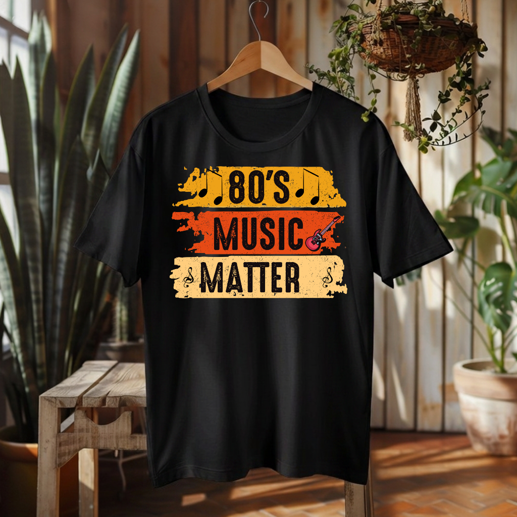 A black short-sleeve t-shirt hanging on a wooden hanger against a rustic wood-paneled wall with plants and a bench. The shirt features a distressed graphic that reads '80's MUSIC MATTER' in black text over yellow, orange, and beige horizontal stripes.