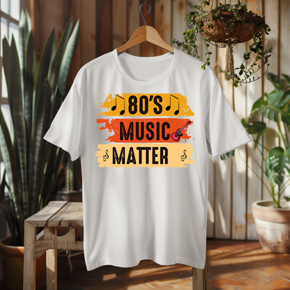 A white short-sleeve T-shirt hanging on a wooden hanger in a rustic indoor setting. The shirt features a colorful retro graphic with the text '80'S MUSIC MATTER' in black over yellow, orange, and beige paint-stroke blocks, with small musical notes and a guitar illustration.