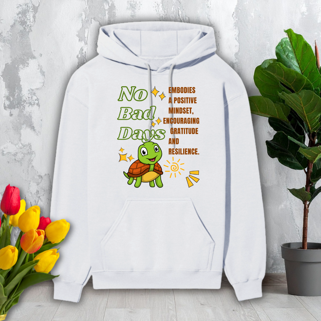 White hoodie with a turtle graphic and motivational text on a light gray background with flowers and a plant.