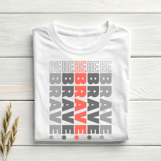 White t-shirt with 'BE BRAVE' text design on a wooden surface