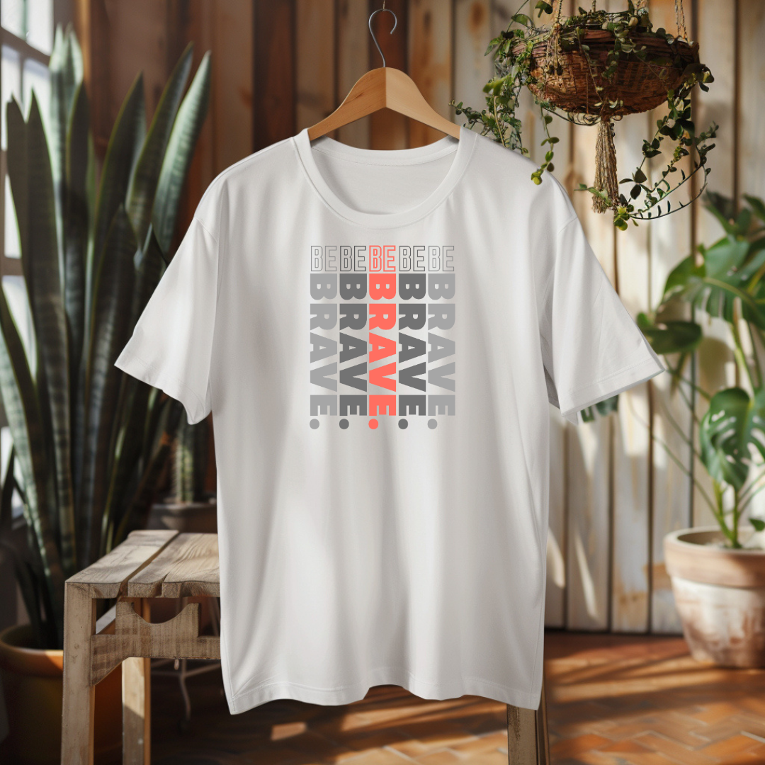 White t-shirt with 'Be Brave' text design on a wooden hanger against a home interior background.