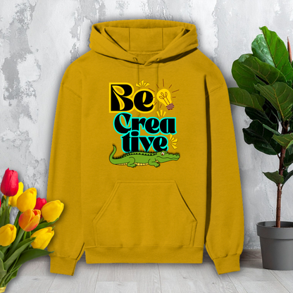 Yellow hoodie with 'Be Creative' text and alligator graphic on a light gray background with flowers and a plant.