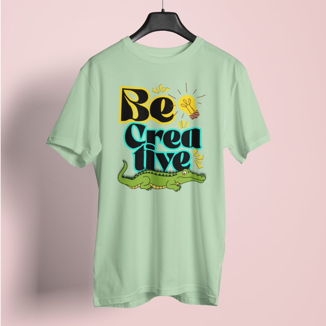 Light green t-shirt with 'Be Creative' text and alligator graphic on a pink background