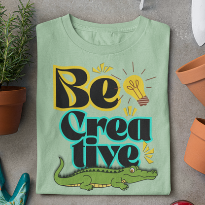 Green t-shirt with 'Be Creative' text and alligator graphic on a gray surface.
