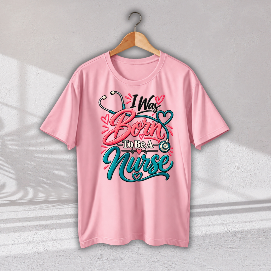 A light pink short-sleeve t-shirt hanging on a wooden hanger against a light gray wall. The shirt features a graphic print on the front with the text 'I Was Born To Be A Nurse' in stylized pink and teal lettering, decorated with a stethoscope and heart motifs.