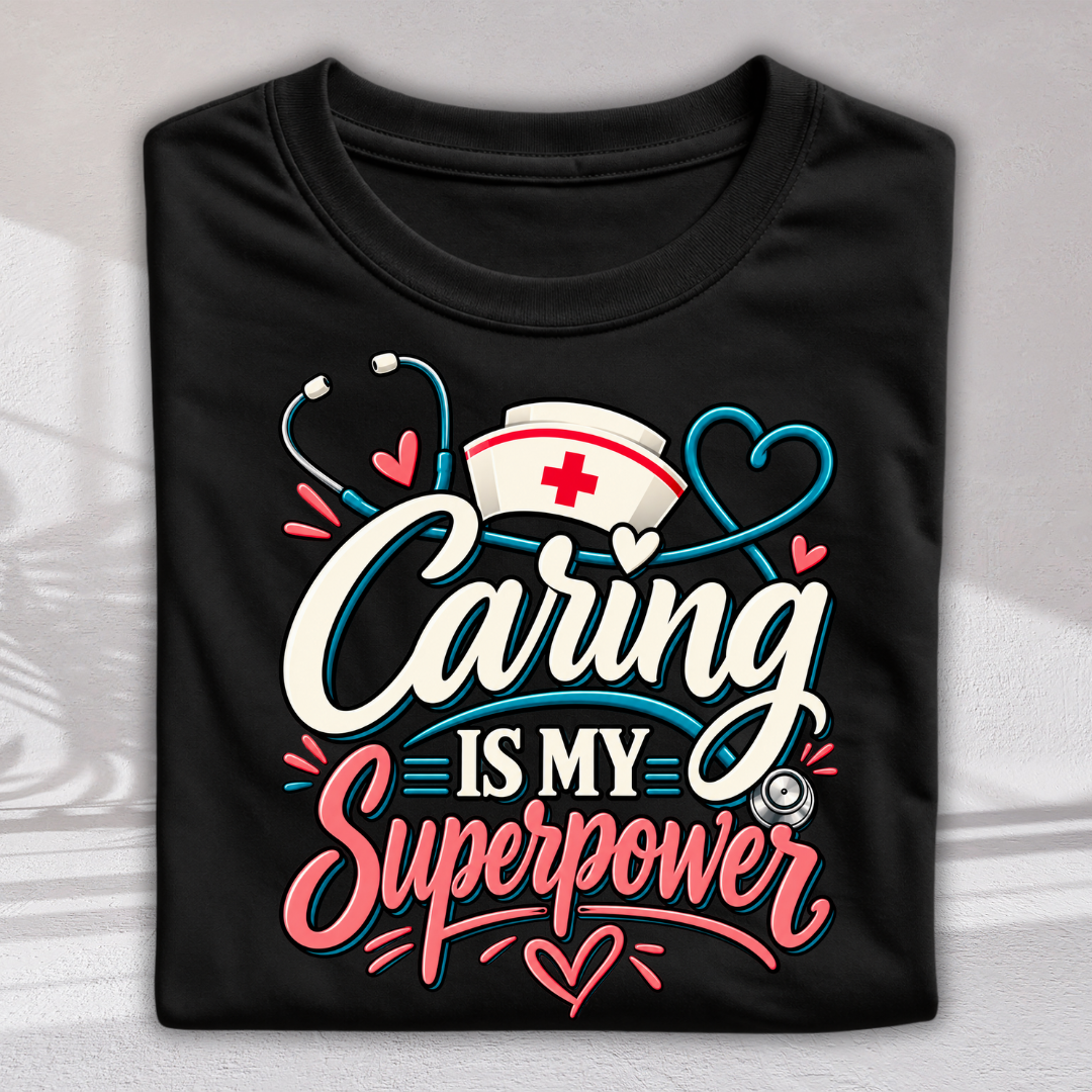 A black folded T-shirt with a colorful graphic that reads 'Caring is my superpower' in white, pink, and blue lettering, decorated with a nurse hat, stethoscope, and hearts, shown on a light gray background.