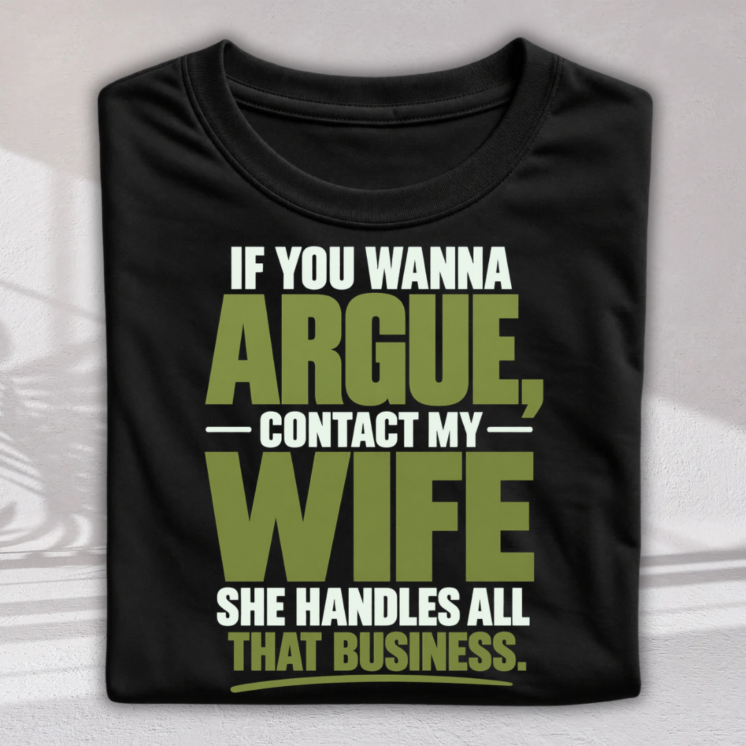 A folded black t-shirt with a humorous text graphic reading 'IF YOU WANNA ARGUE, CONTACT MY WIFE SHE HANDLES ALL THAT BUSINESS.' in white and olive green lettering, displayed against a light gray background with soft shadows.