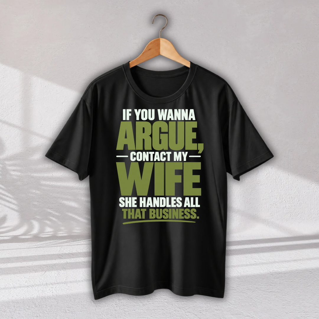 A black short-sleeve graphic T-shirt hanging on a wooden hanger against a light gray wall. The shirt features a bold text graphic in white and olive green that reads, 'IF YOU WANNA ARGUE, CONTACT MY WIFE SHE HANDLES ALL THAT BUSINESS.