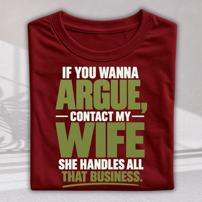 A folded dark red t-shirt with a humorous text graphic reading 'IF YOU WANNA ARGUE, CONTACT MY WIFE SHE HANDLES ALL THAT BUSINESS.' in white and olive green lettering, displayed on a light gray background.