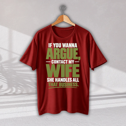 A red short-sleeve graphic T-shirt hanging on a wooden hanger against a light gray wall. The shirt features a bold text graphic in white and olive green that reads, 'IF YOU WANNA ARGUE, CONTACT MY WIFE SHE HANDLES ALL THAT BUSINESS.