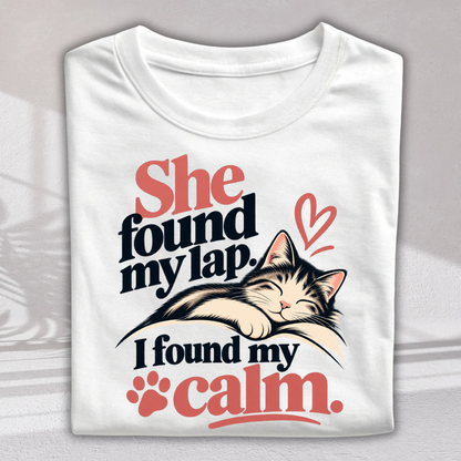 A folded white short-sleeve T-shirt with a printed graphic of a sleeping cat and the text 'She found my lap. I found my calm.