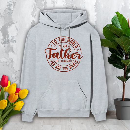 Gray hoodie with red text 'To the world you are a Father but to our family you are the world' on a light gray background with flowers and a plant.