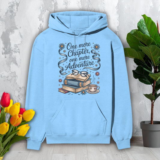 Light blue hoodie with book-themed design and text, placed on a surface with flowers and a plant.