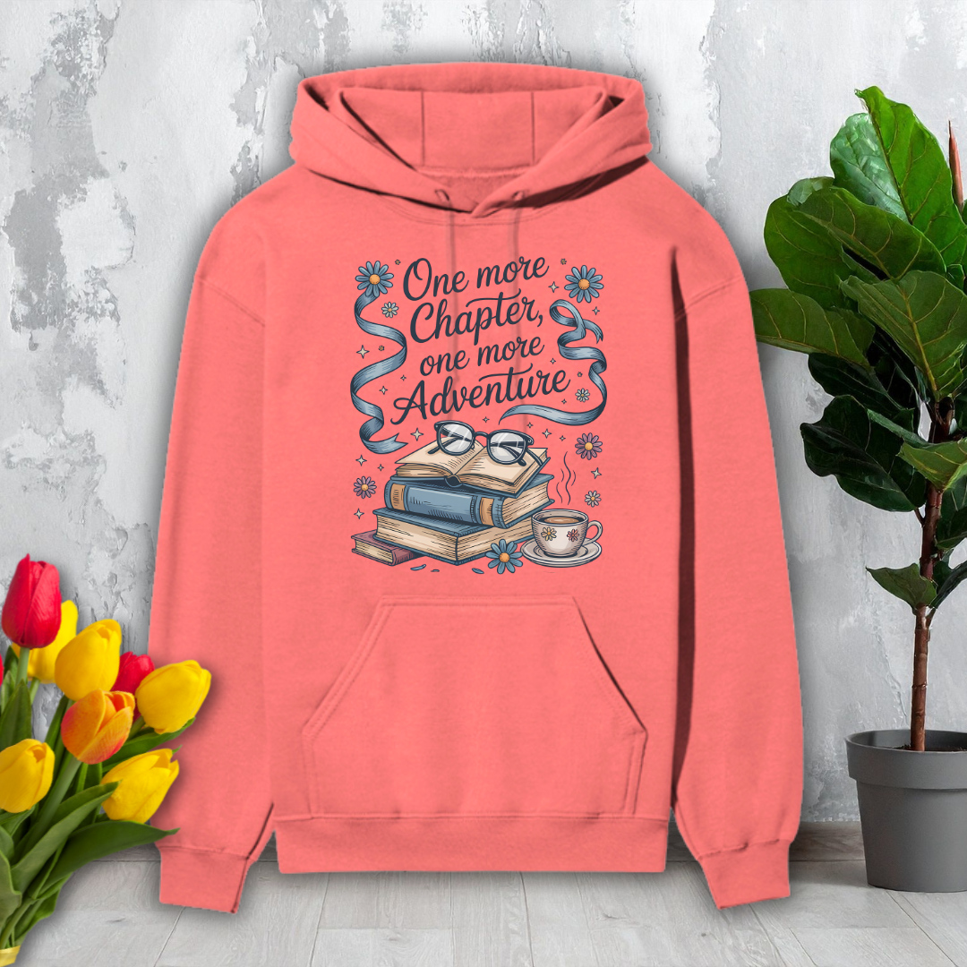Coral hoodie with book-themed design on a light gray surface with flowers and a plant.