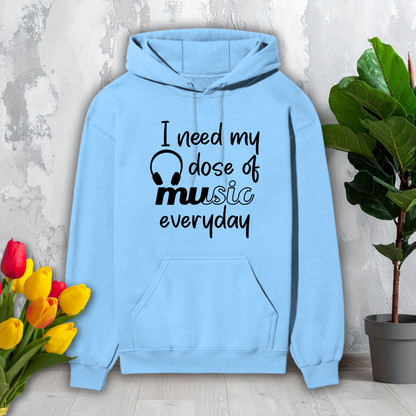 Light blue hoodie with 'I need my dose of music everyday' text on a light gray background with flowers and a plant.