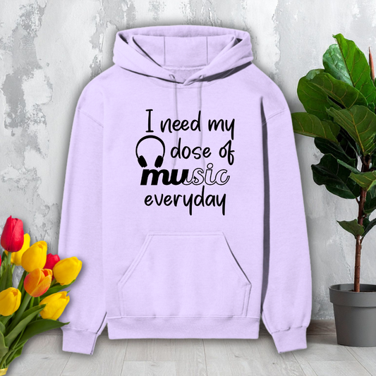 Purple hoodie with text 'I need my dose of music everyday' on a light gray surface with flowers and a plant.