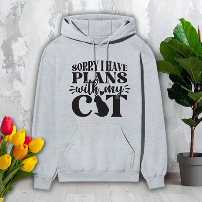 Gray hoodie with text 'Sorry I have plans with my cat' on a light gray background with flowers and a plant.