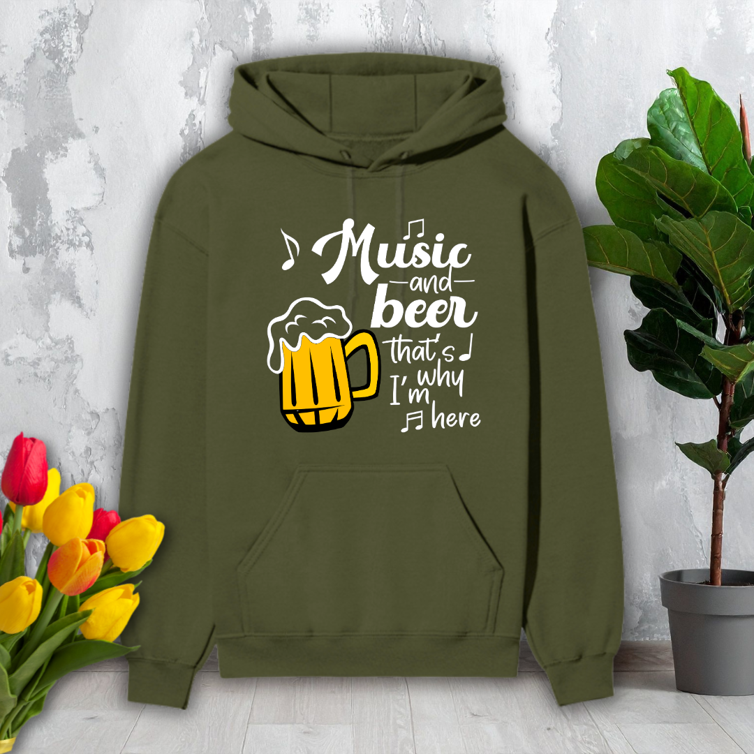 Green hoodie with 'Music and beer that's why I'm here' text and beer mug graphic on a light gray surface with flowers and a plant.