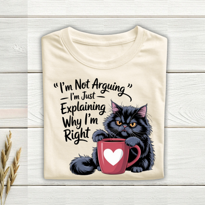 Beige t-shirt with a black cat holding a red mug and humorous text on a wooden surface.