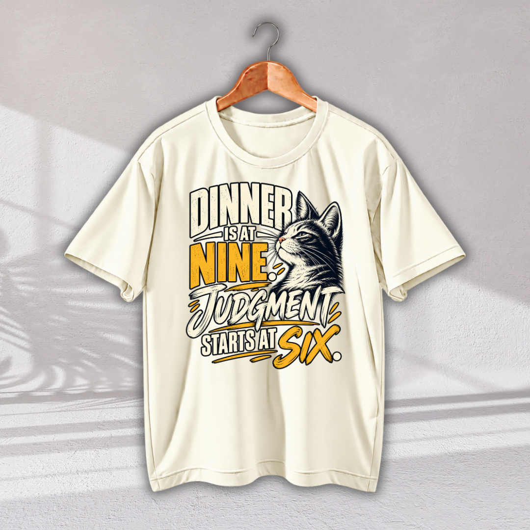 An off-white short-sleeve t-shirt on a wooden hanger, featuring a graphic print of a cat's head and the text 'DINNER IS AT NINE, JUDGMENT STARTS AT SIX.' in yellow, black, and white.