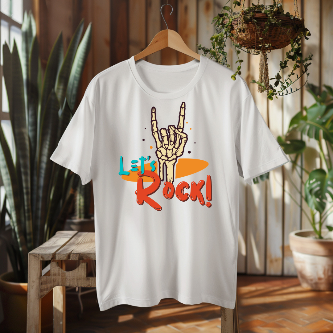 A white short-sleeve t-shirt on a wooden hanger, featuring a graphic of a skeleton hand making the rock on gesture above the text 'Let's Rock!' in orange and teal. The shirt is displayed in a warm, rustic indoor setting with plants and wooden furniture.