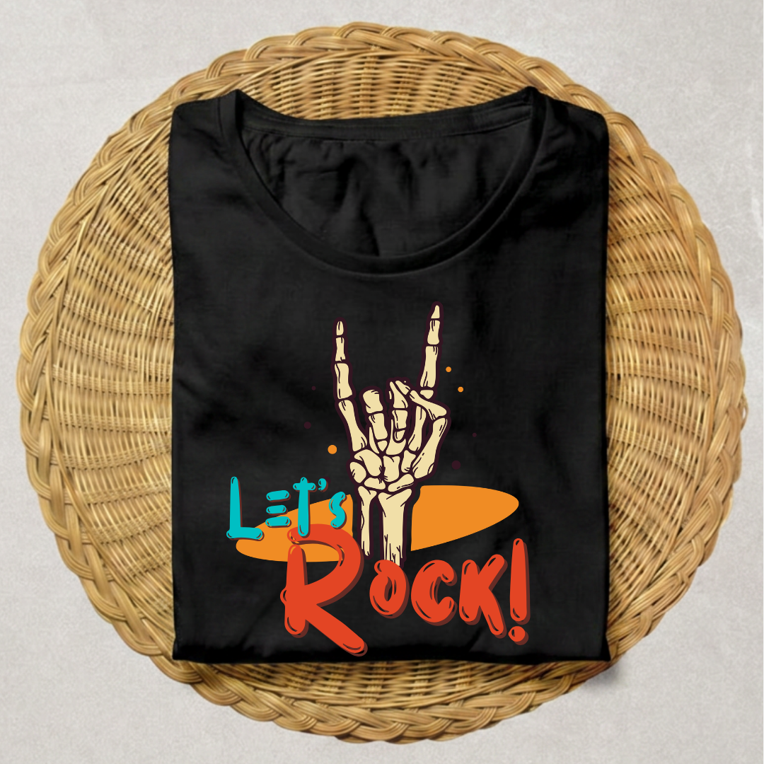 A black short-sleeve t-shirt laid flat on a round woven wicker tray. The shirt features a graphic print of a skeleton hand making the rock on gesture above the text 'Let's Rock!' in orange, red, and blue.