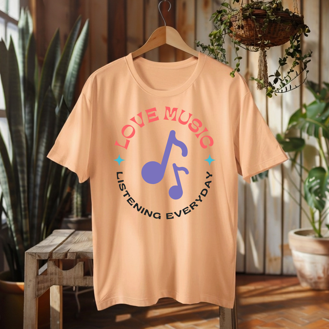 A peach-colored short-sleeve t-shirt hanging on a wooden hanger, featuring a graphic print with the words 'LOVE MUSIC' and 'LISTENING EVERYDAY' in pink and black, surrounding a blue musical note.