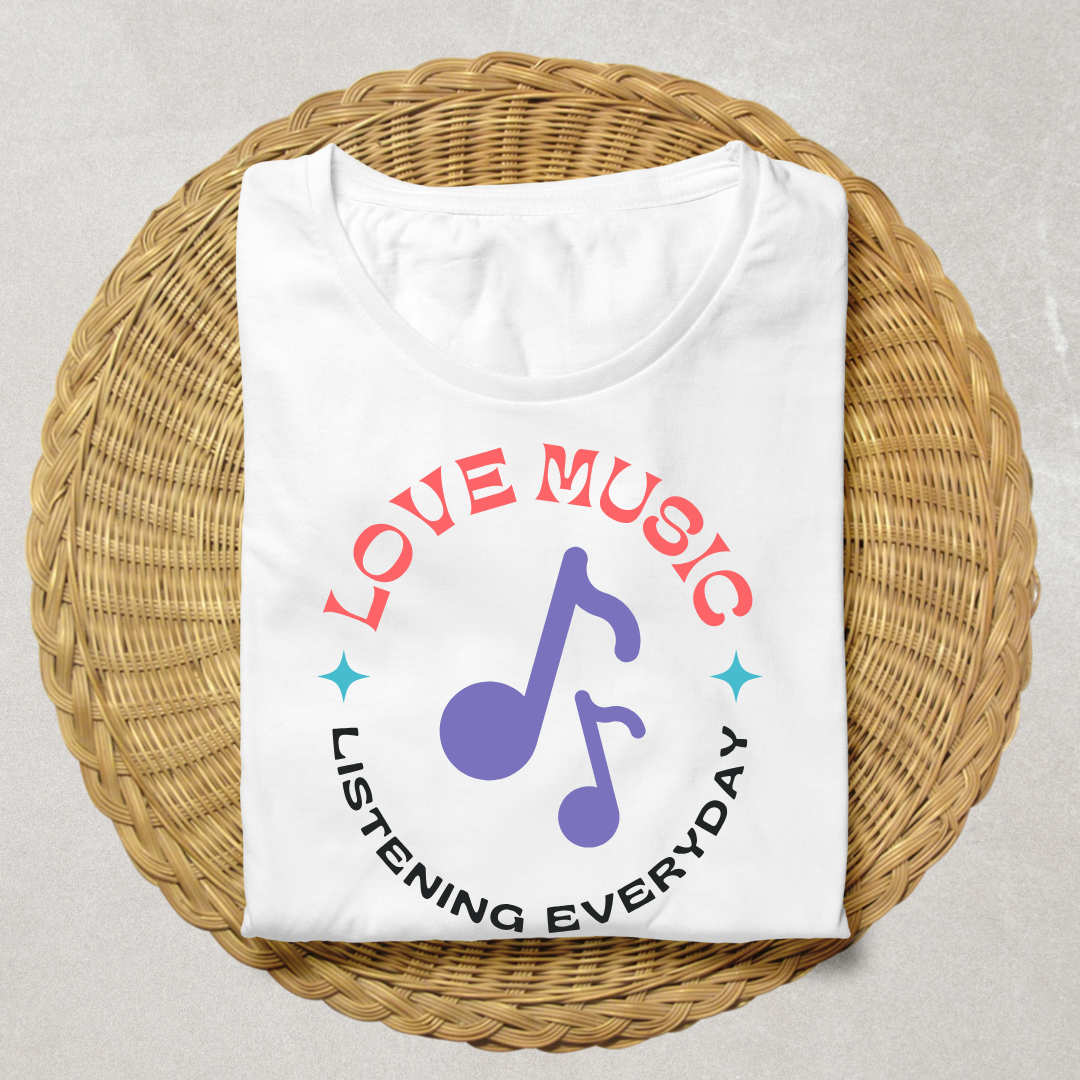 A folded white t-shirt with a colorful graphic print reading 'LOVE MUSIC LISTENING EVERYDAY' around a purple music note, displayed on a round woven straw mat against a light gray background.