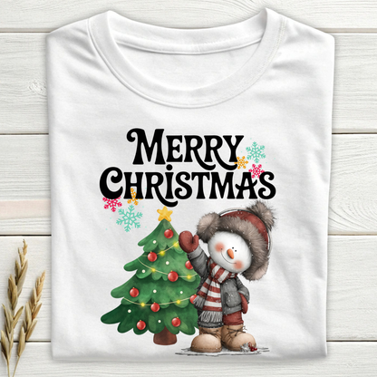 White t-shirt with a snowman and Christmas tree design on a wooden surface