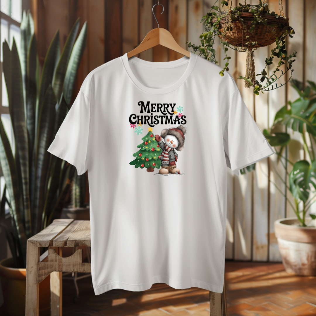 White t-shirt with Christmas design featuring a snowman and tree, hanging on a wooden hanger.