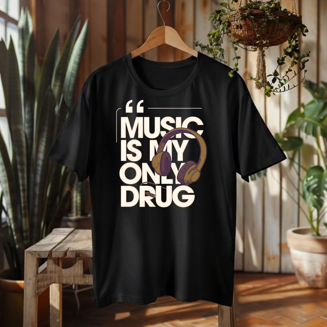 A black short-sleeve graphic t-shirt hanging on a wooden hanger in a rustic indoor setting. The shirt features a bold graphic print that reads 'MUSIC IS MY ONLY DRUG' in white, with a graphic of gold and purple headphones layered over the text.