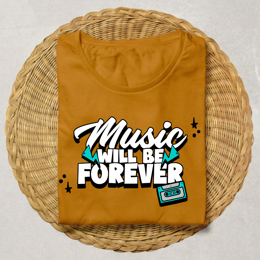 A folded mustard yellow t-shirt with a retro graphic reading 'Music WILL BE FOREVER' in white and black, accented with teal triangles and a cassette tape illustration, displayed on a round woven wicker tray.
