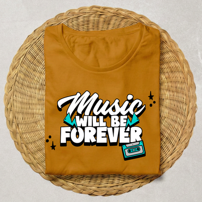 A folded mustard yellow t-shirt with a retro graphic reading 'Music WILL BE FOREVER' in white and black, accented with teal triangles and a cassette tape illustration, displayed on a round woven wicker tray.