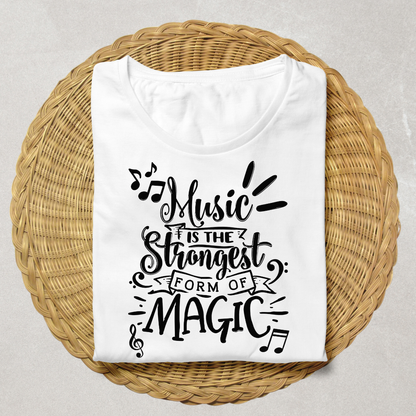 A folded white t-shirt with a black graphic text reading 'Music is the strongest form of magic' and musical notes, displayed on a round woven wicker tray against a light gray background.
