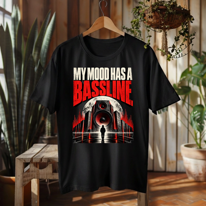 A black graphic t-shirt hanging on a wooden hanger in a rustic indoor setting. The shirt features a graphic print with the text 'MY MOOD HAS A BASSLINE.
