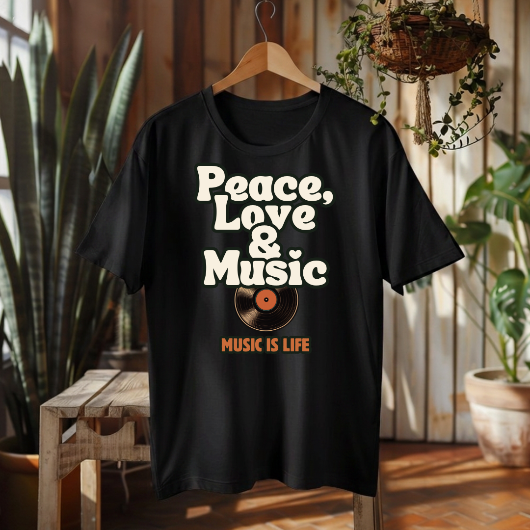 A black short-sleeve graphic T-shirt hanging on a wooden hanger in a rustic indoor setting. The shirt features the words 'Peace, Love & Music' in large white retro-style lettering above a vinyl record graphic with an orange center, and 'MUSIC IS LIFE' in orange text below.