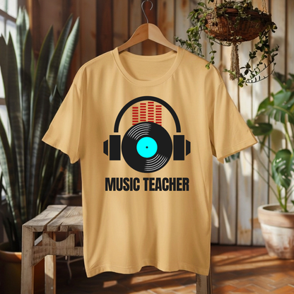 A light beige graphic t-shirt hanging on a wooden hanger against a rustic wood-paneled wall with plants. The shirt features a graphic of black headphones over a vinyl record with a bright cyan center and red audio bars, with the text 'MUSIC TEACHER' printed below in black.