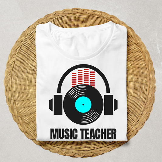 A folded white t-shirt displayed on a round woven straw mat. The shirt features a graphic of black headphones with a vinyl record and red equalizer bars, with the text 'MUSIC TEACHER' printed below in black.
