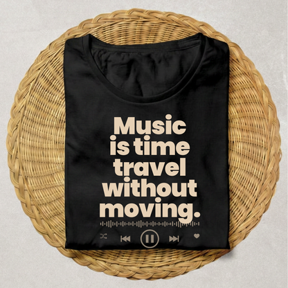 A black short-sleeve T-shirt laid flat on a round woven wicker tray, with large cream text reading 'Music is time travel without moving.' and small music-player interface icons along the bottom.