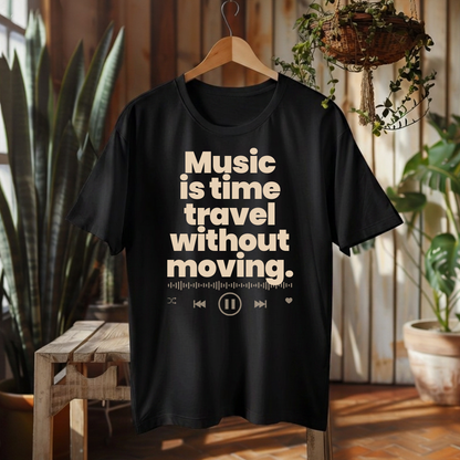 A black short-sleeve graphic T-shirt hanging on a wooden hanger in a rustic indoor setting with plants and wood paneling. The shirt features a cream-colored text graphic that reads 'Music is time travel without moving.