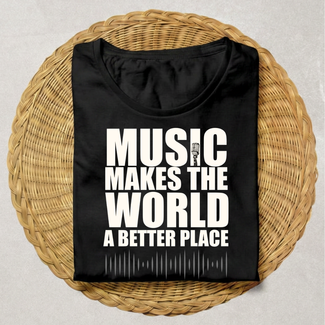 A black short-sleeve T-shirt with bold white text reading 'MUSIC MAKES THE WORLD A BETTER PLACE' and a small microphone graphic, laid flat on a round woven wicker tray against a light gray background.