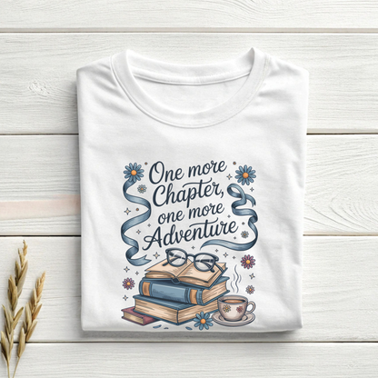 White t-shirt with book-themed design and text 'One more Chapter, one more Adventure' on a wooden surface.