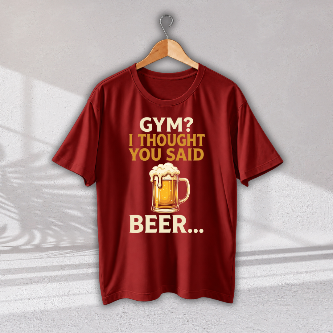 A dark red short-sleeve t-shirt hanging on a wooden hanger against a light gray wall. The shirt features a graphic print with the text 'GYM? I THOUGHT YOU SAID BEER.