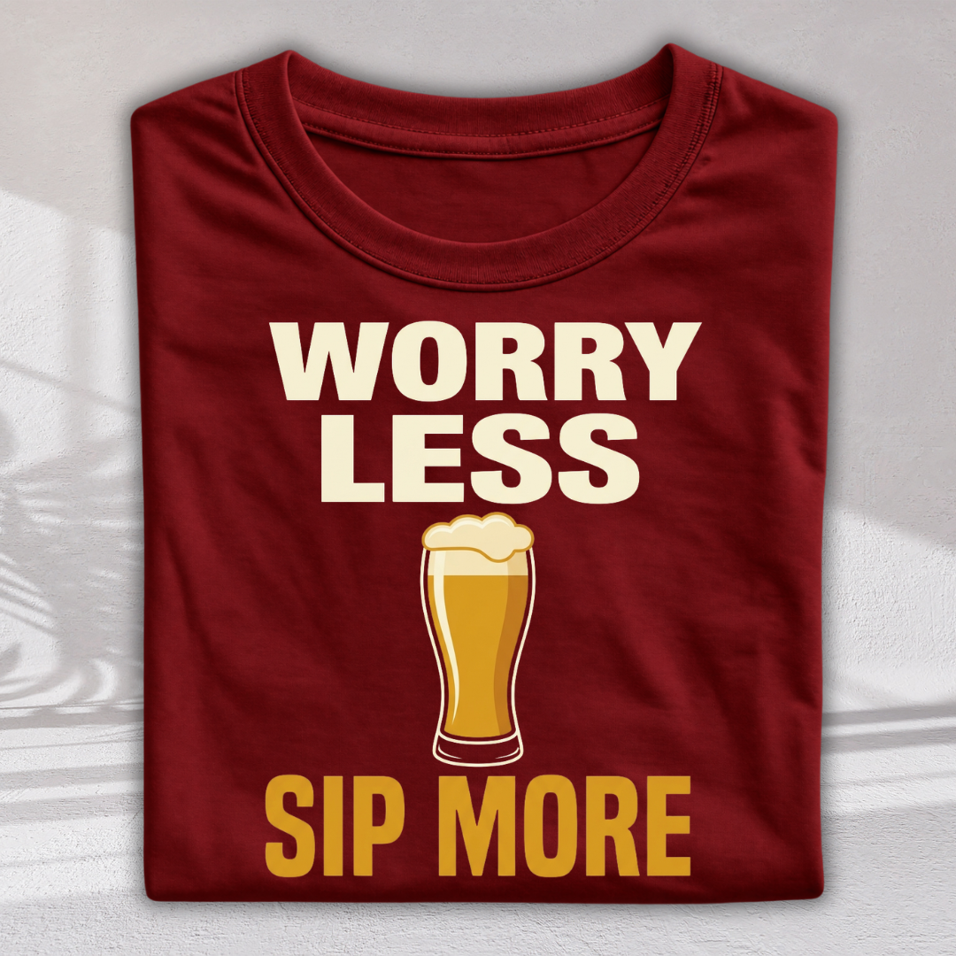 A folded maroon t-shirt with a graphic print that reads 'WORRY LESS SIP MORE' in cream and yellow text, featuring an illustration of a pint of beer in the center, displayed against a light gray background with soft shadow overlays.