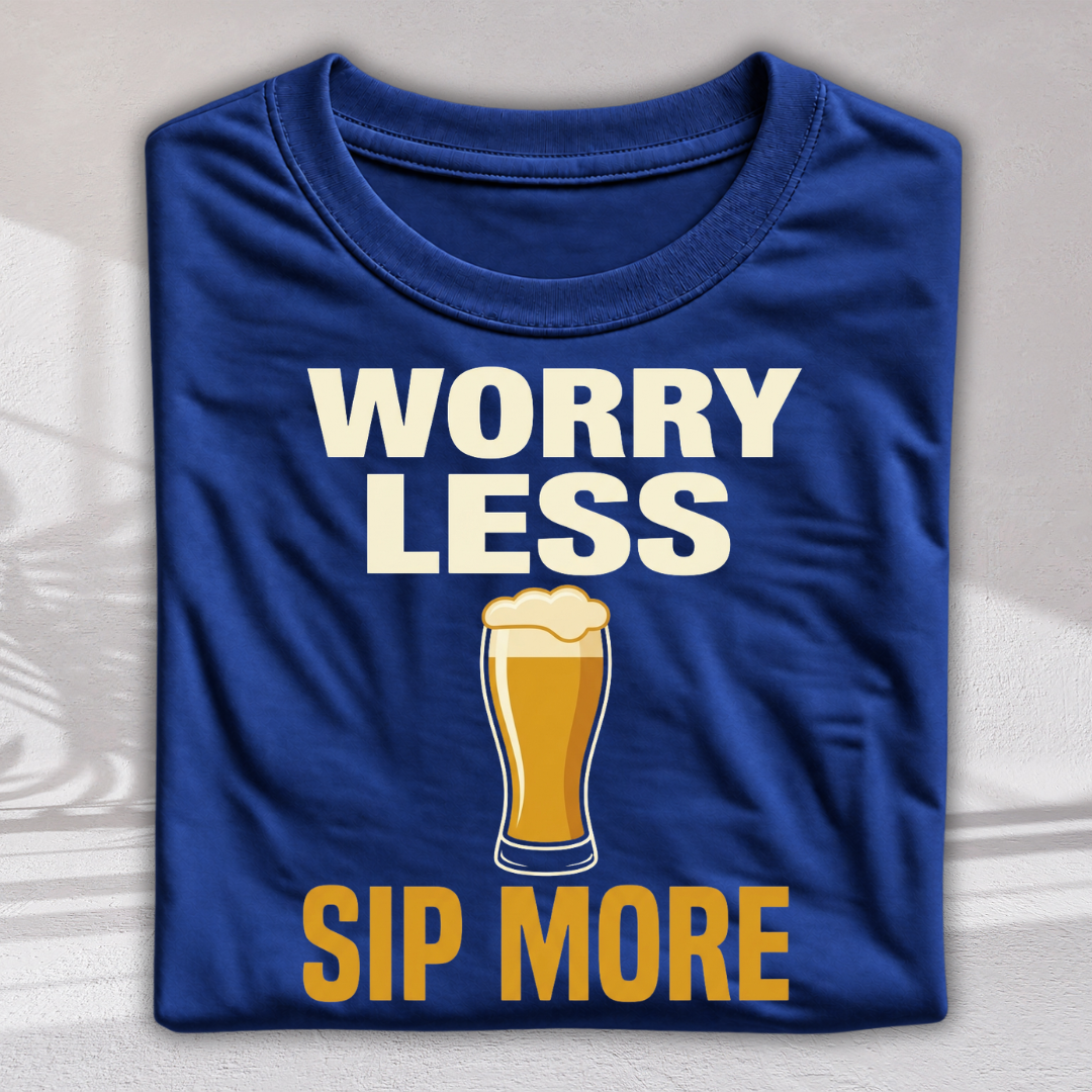 A folded royal blue t-shirt with a graphic print that reads 'WORRY LESS SIP MORE' in white and yellow text, featuring an illustration of a pint of beer in the center, displayed on a light gray textured background.