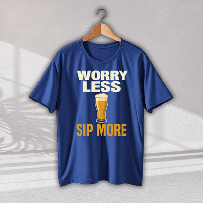 A royal blue short-sleeve t-shirt hanging on a wooden hanger against a light gray wall. The shirt features a graphic print with the text 'WORRY LESS SIP MORE' in white and yellow, surrounding an illustration of a beer glass.