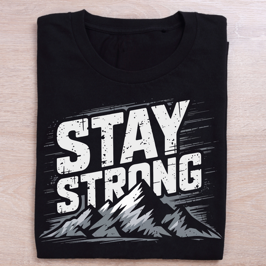 Black t-shirt with 'Stay Strong' text and mountain graphic on a wooden surface