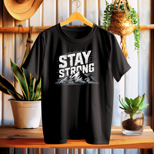 Black t-shirt with 'Stay Strong' text on a wooden surface with plants in the background
