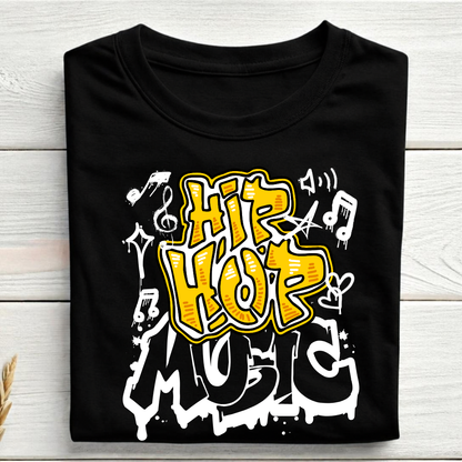 A black short-sleeve T-shirt laid flat on a light wood plank background, featuring a large graffiti-style graphic that reads 'HIP HOP MUSIC' in yellow, white, and black, with musical notes and symbols.
